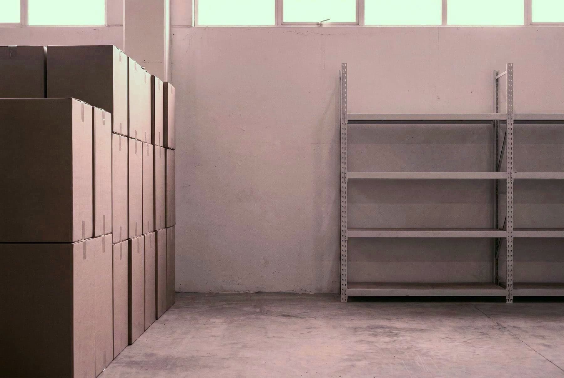 Pusta półka magazynowa obok kolumny kartonów, zwolniona pod nowy model